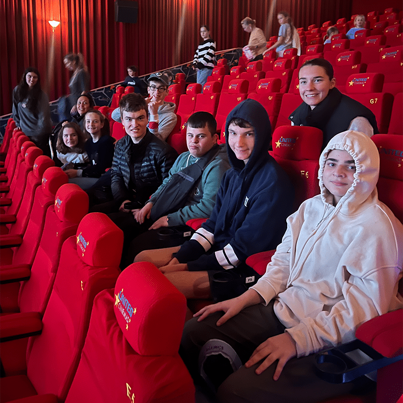 A group of people sitting in a row of seats at a movie theatre, smiling to camera.